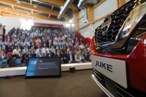Presentación corporativa de Nissan con vehículo en primer plano y asistentes en un auditorio.
