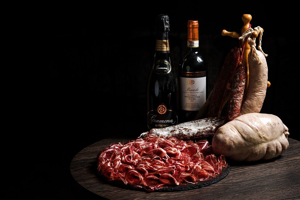 Composición de producto gastronómico con embutidos, carne curada y botellas de vino sobre una mesa oscura.