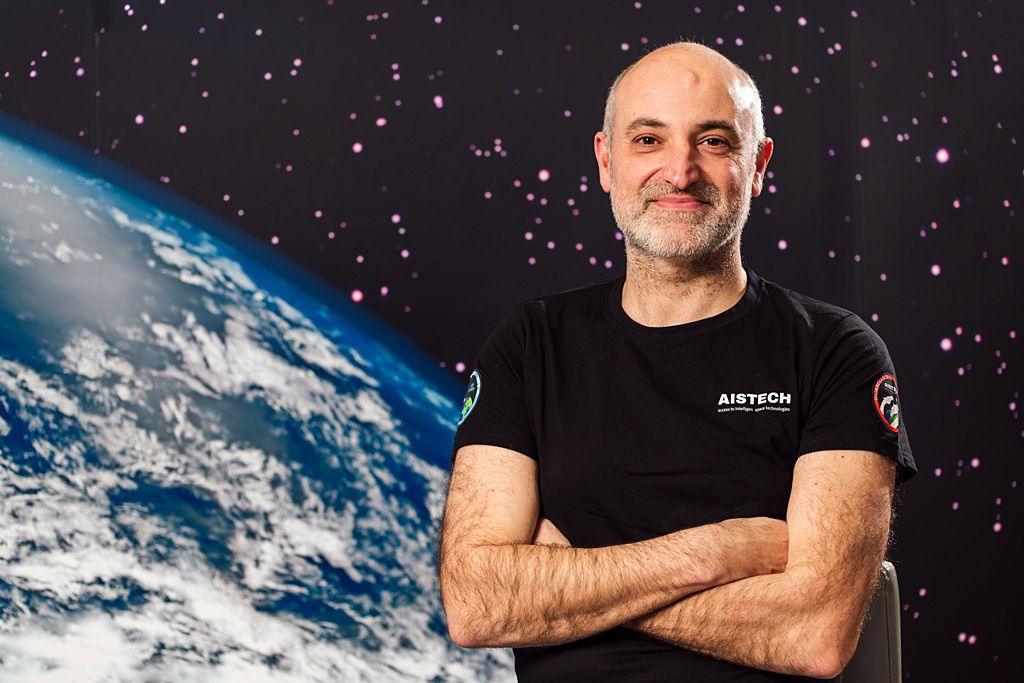 Retrato de un profesional con camiseta corporativa, sonriendo con los brazos cruzados frente a un fondo gráfico con la Tierra vista desde el espacio.