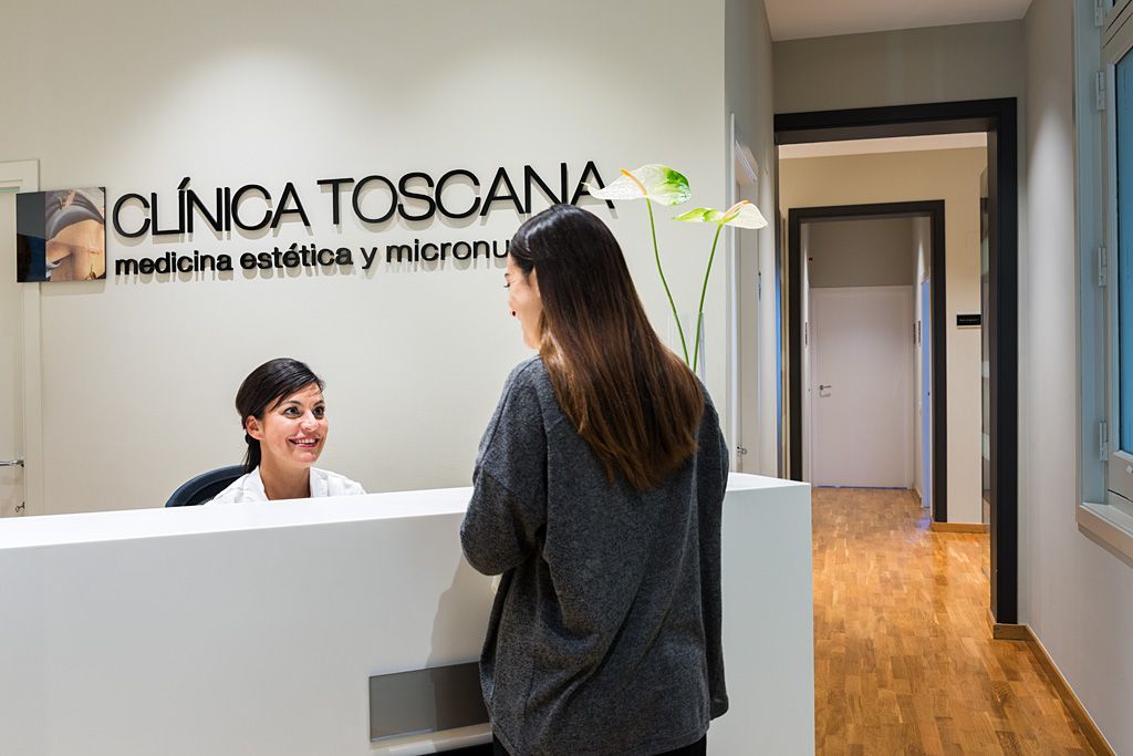 Recepción de una clínica estética con una profesional atendiendo a una paciente en el mostrador, junto a la identidad visual del centro.