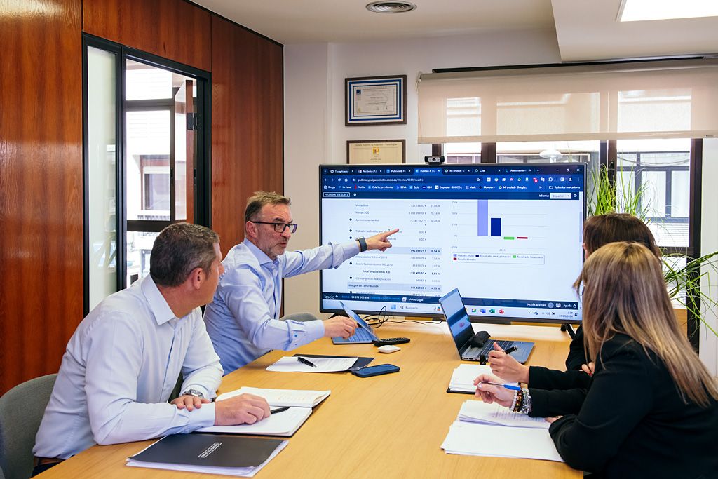 Equipo reunido en un despacho profesional analizando datos financieros en una pantalla, con ordenadores portátiles y documentación sobre la mesa.