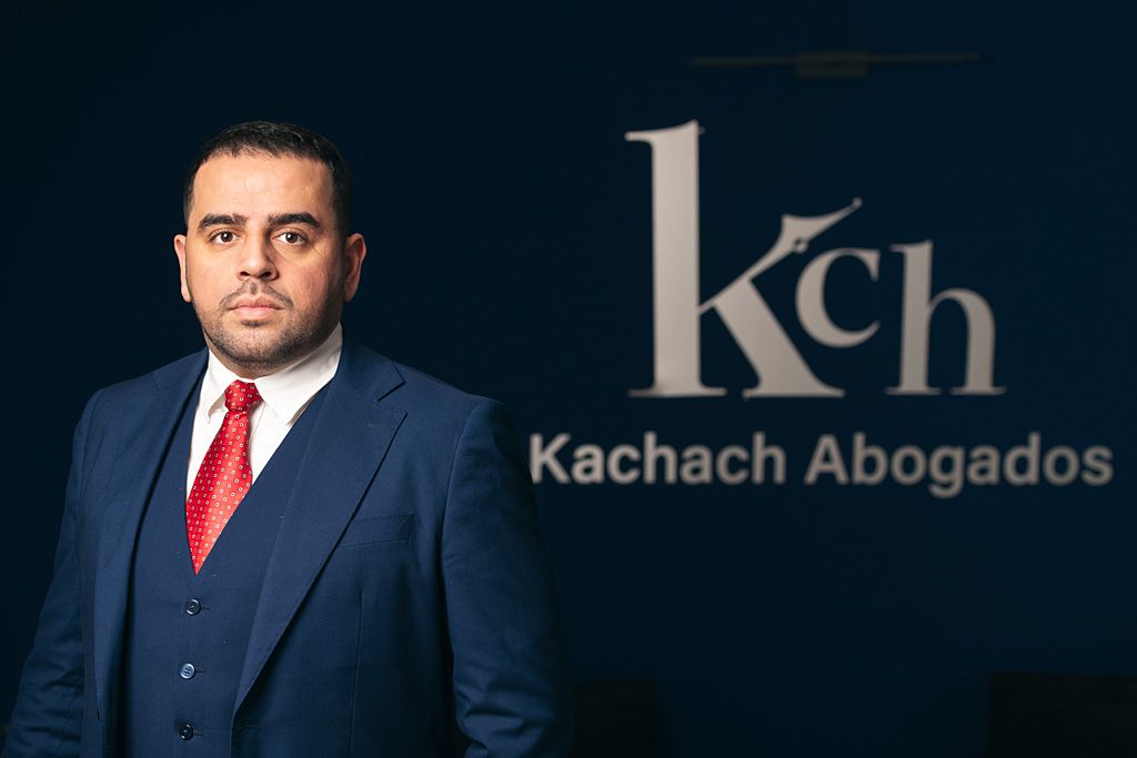 Retrato corporativo de un profesional en un despacho de abogados con la marca visible al fondo.