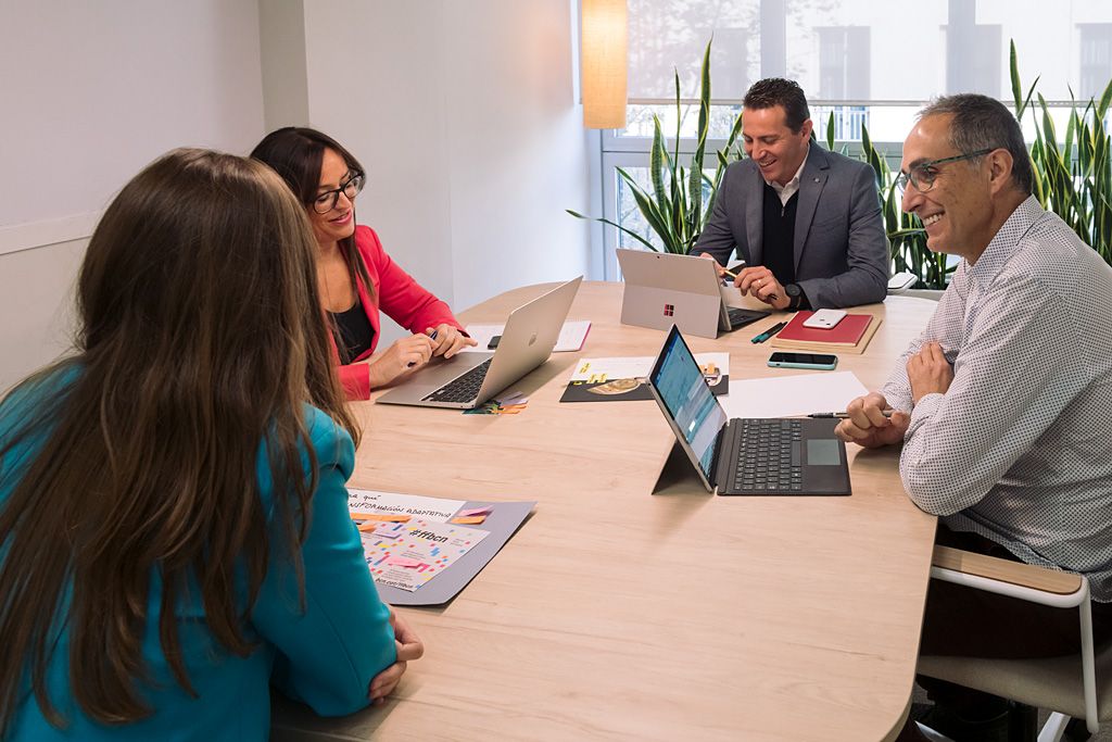 Equipo profesional reunido alrededor de una mesa de trabajo con portátiles y documentos en un contexto de consultoría B2B.